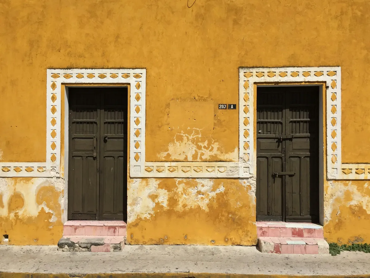 A yellow colonial house front with two dark wooden doors and white trim