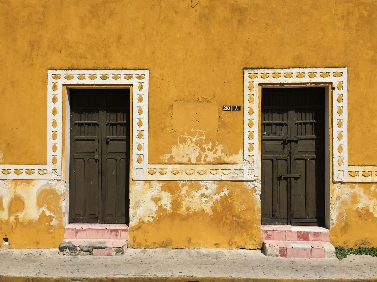 A yellow colonial house front with two dark wooden doors and white trim
