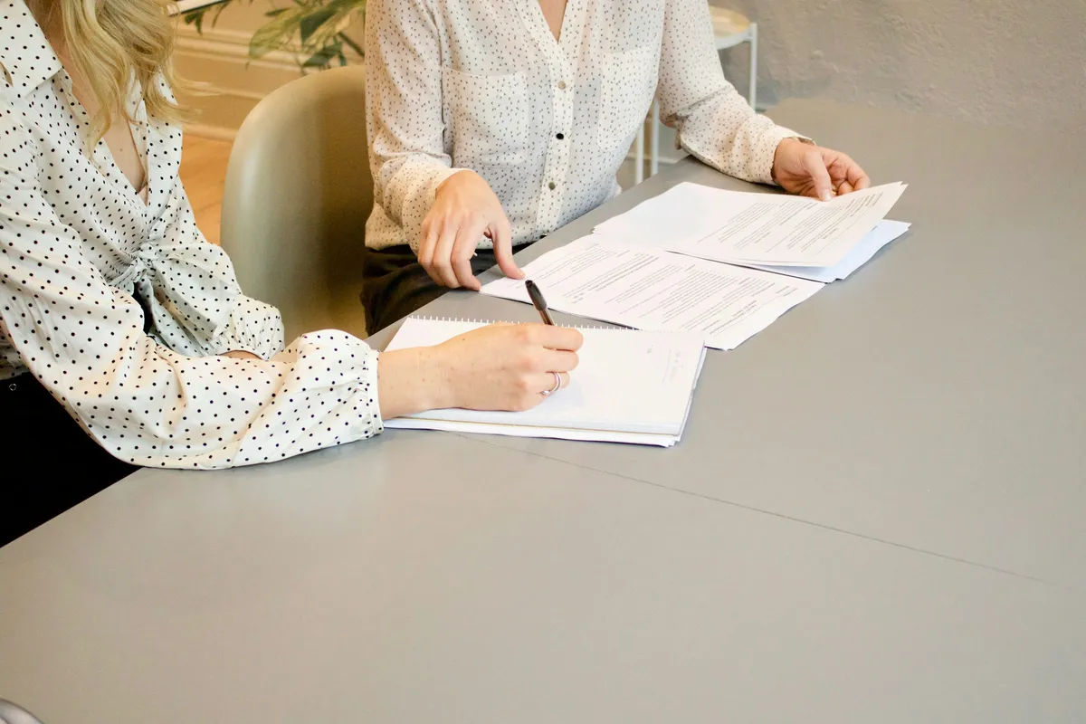 Two people at a table, one signing a document